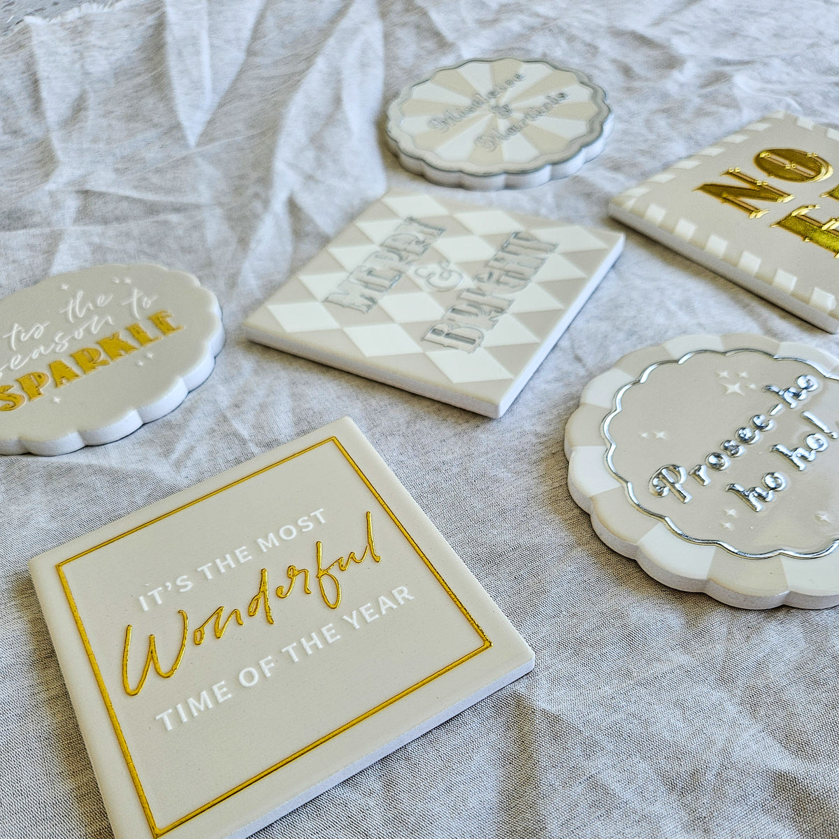 Angled view of the six Merry Sparkle ceramic coasters with festive lettering and metallic details