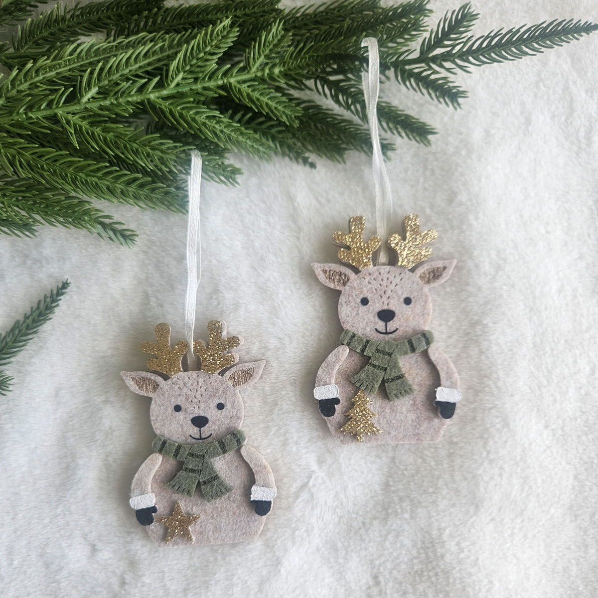 Two felt reindeer Christmas ornaments with sage green scarves, glittery gold antlers and little star details