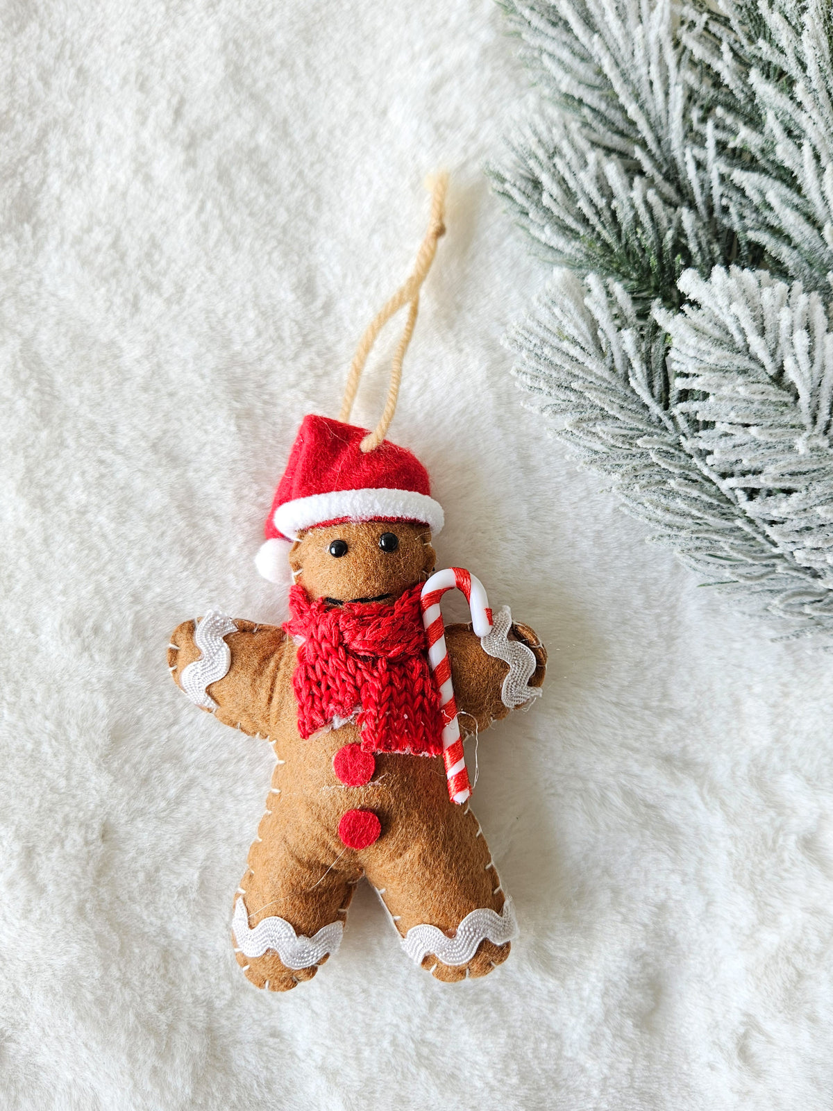 Gingerbread ornament wearing a red Santa hat and knitted scarf, holding a striped candy cane
