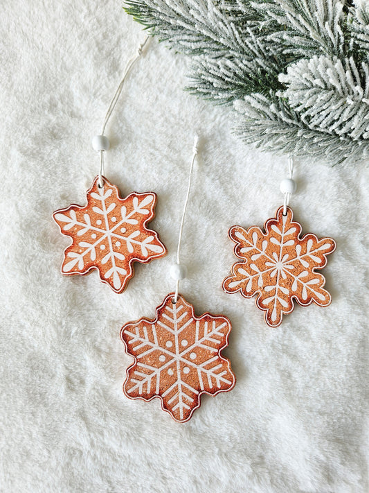 Three brown wooden snowflake ornaments with white icing-style patterns and white hanging cords