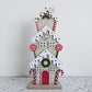 Three-storey wooden gingerbread townhouse with white icing details, a red door and candy cane decorations