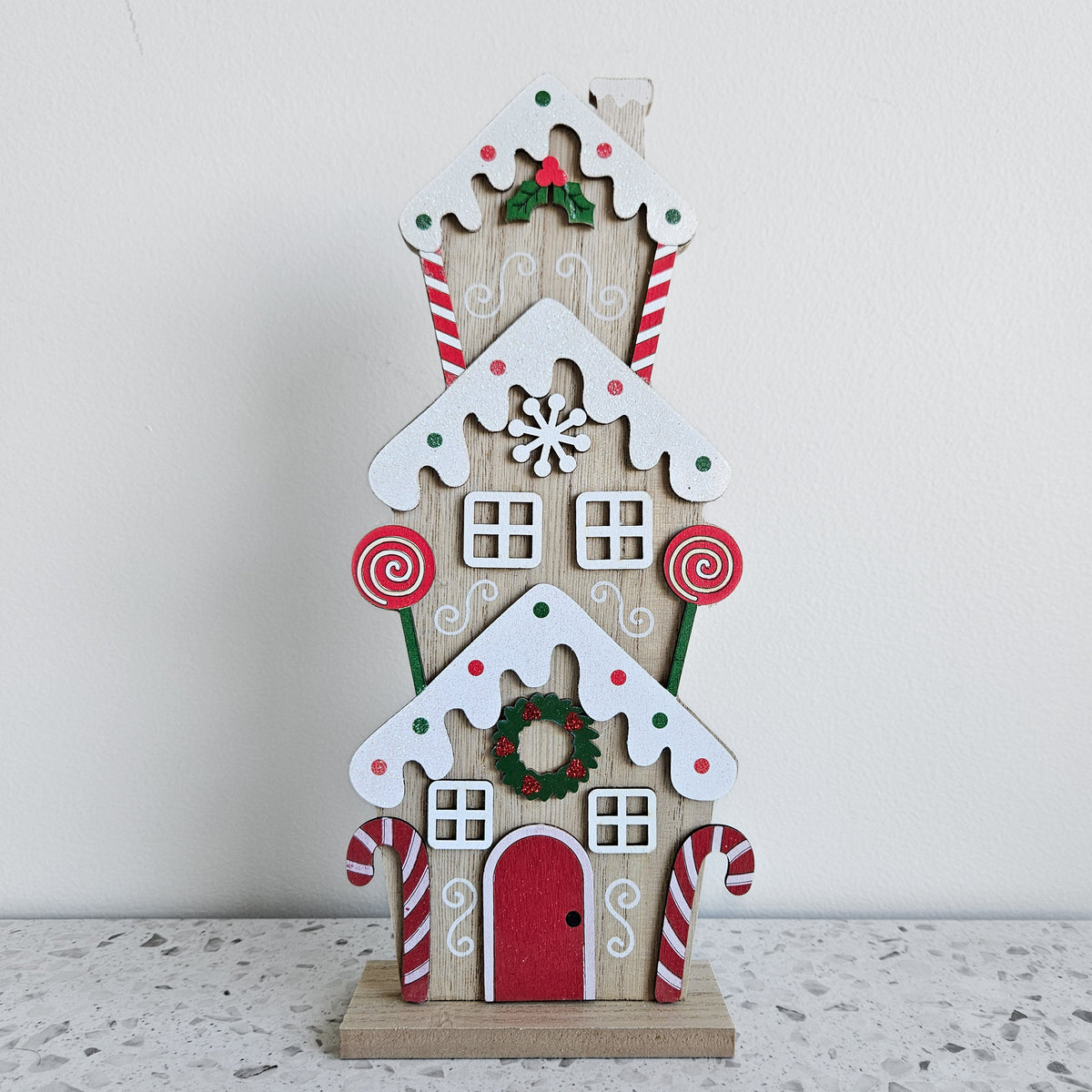 Three-storey wooden gingerbread townhouse with white icing details, a red door and candy cane decorations