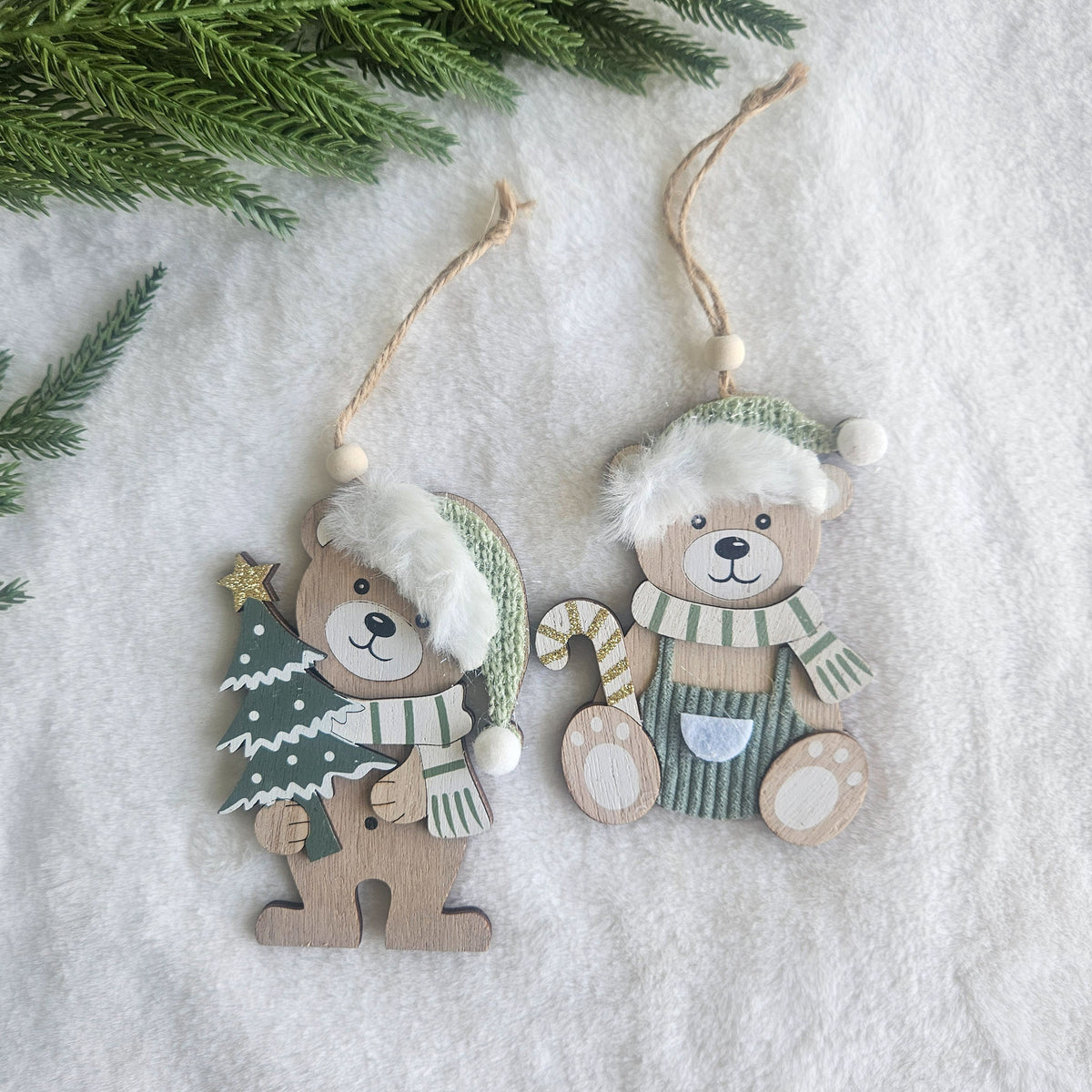 Two wooden teddy bear Christmas ornaments in sage green hats and scarves, one holding a tree and one holding a candy cane