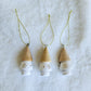 Close-up of three white hanging tree ornaments with gold snowflakes, natural-toned tops and gold cords