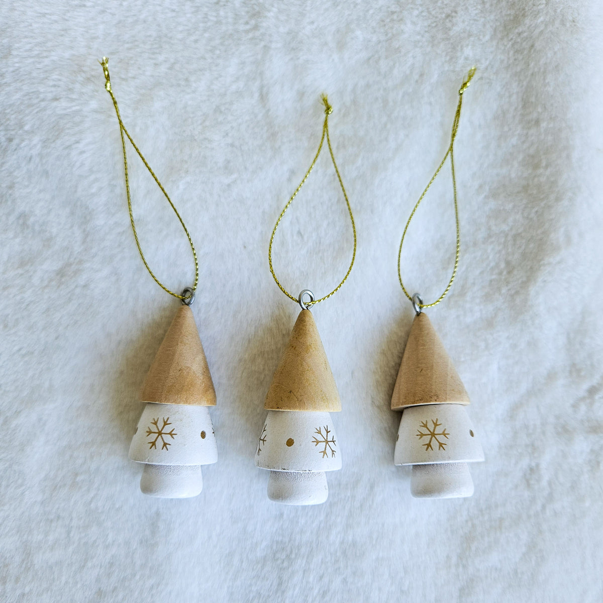 Close-up of three white hanging tree ornaments with gold snowflakes, natural-toned tops and gold cords